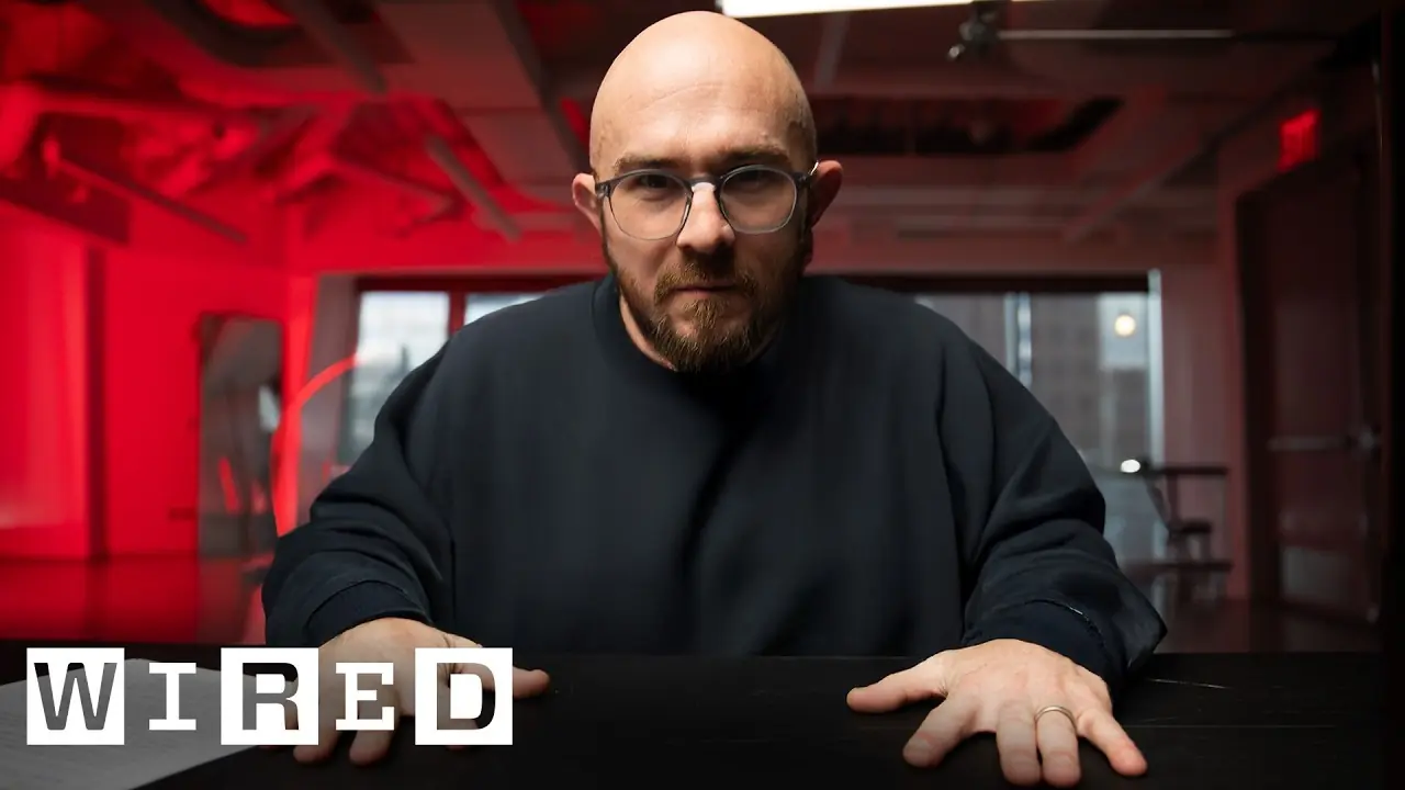 A man looking very serious in a dark room with a red glow lighting the room.